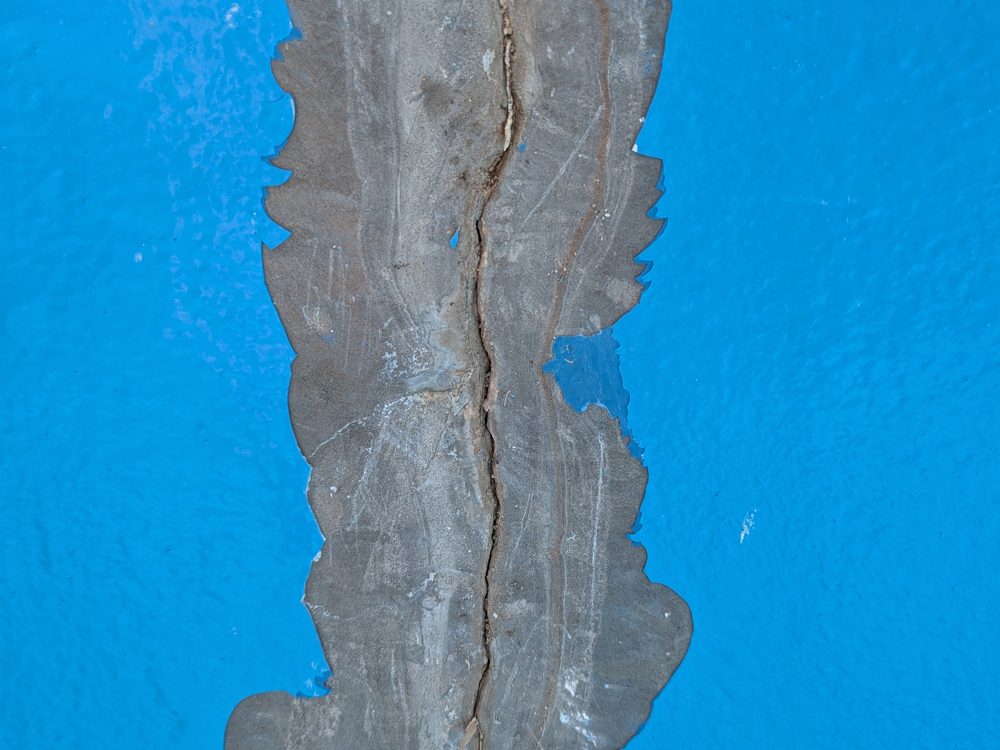 Paint lifting along a crack in a painted concrete pool wall
