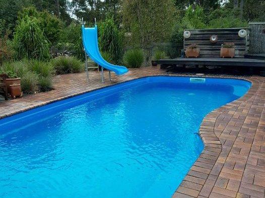 Freeform pool resurfaced in blue, filled, with a water slide