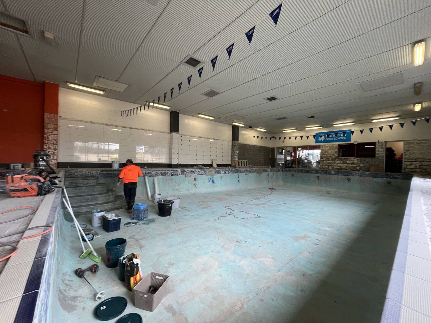 Wide view of an indoor commercial pool being prepared, with crew and equipment