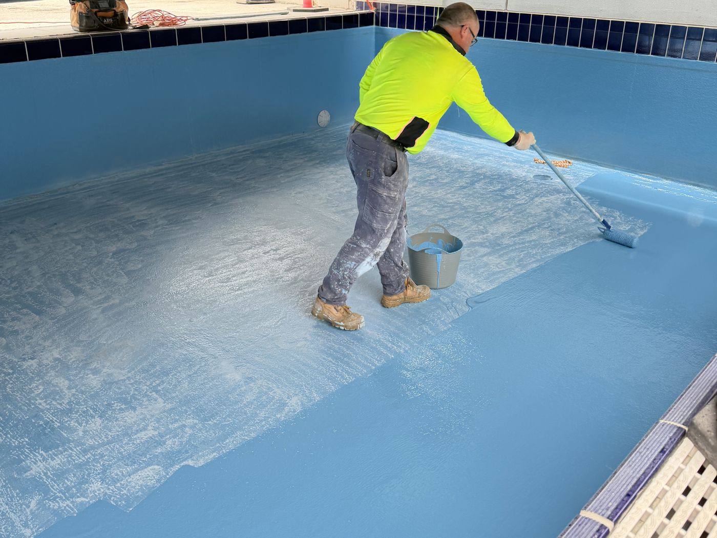 APR crew member rolling out topcoat across a pool floor during a fibreglass resurface