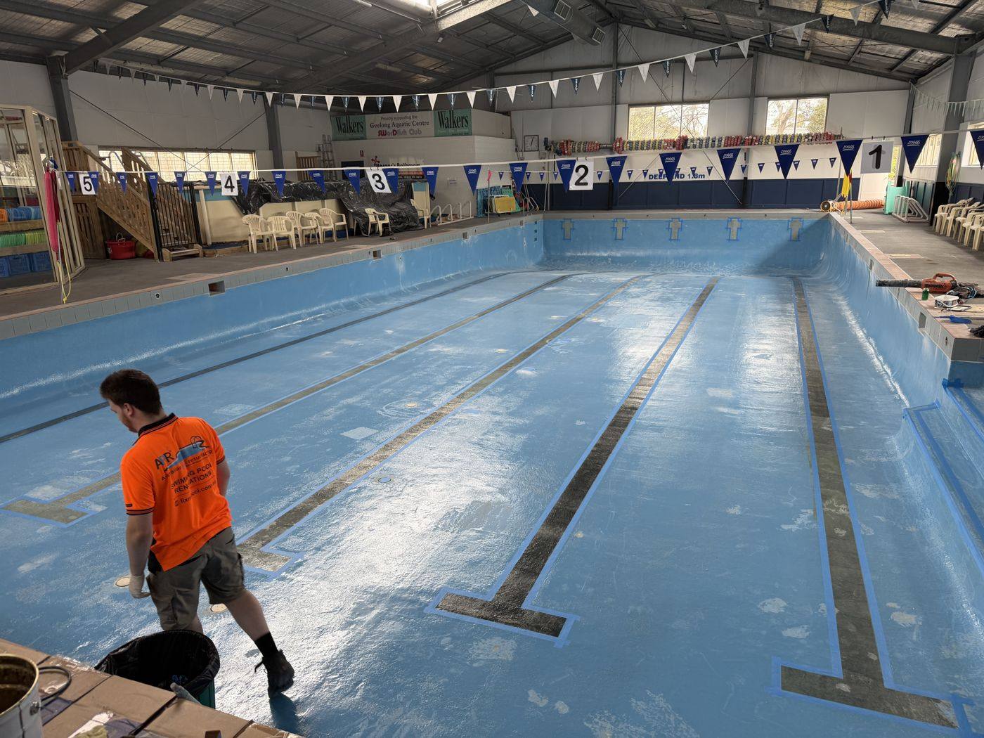 Crew member working in an empty indoor swim school pool during resurfacing